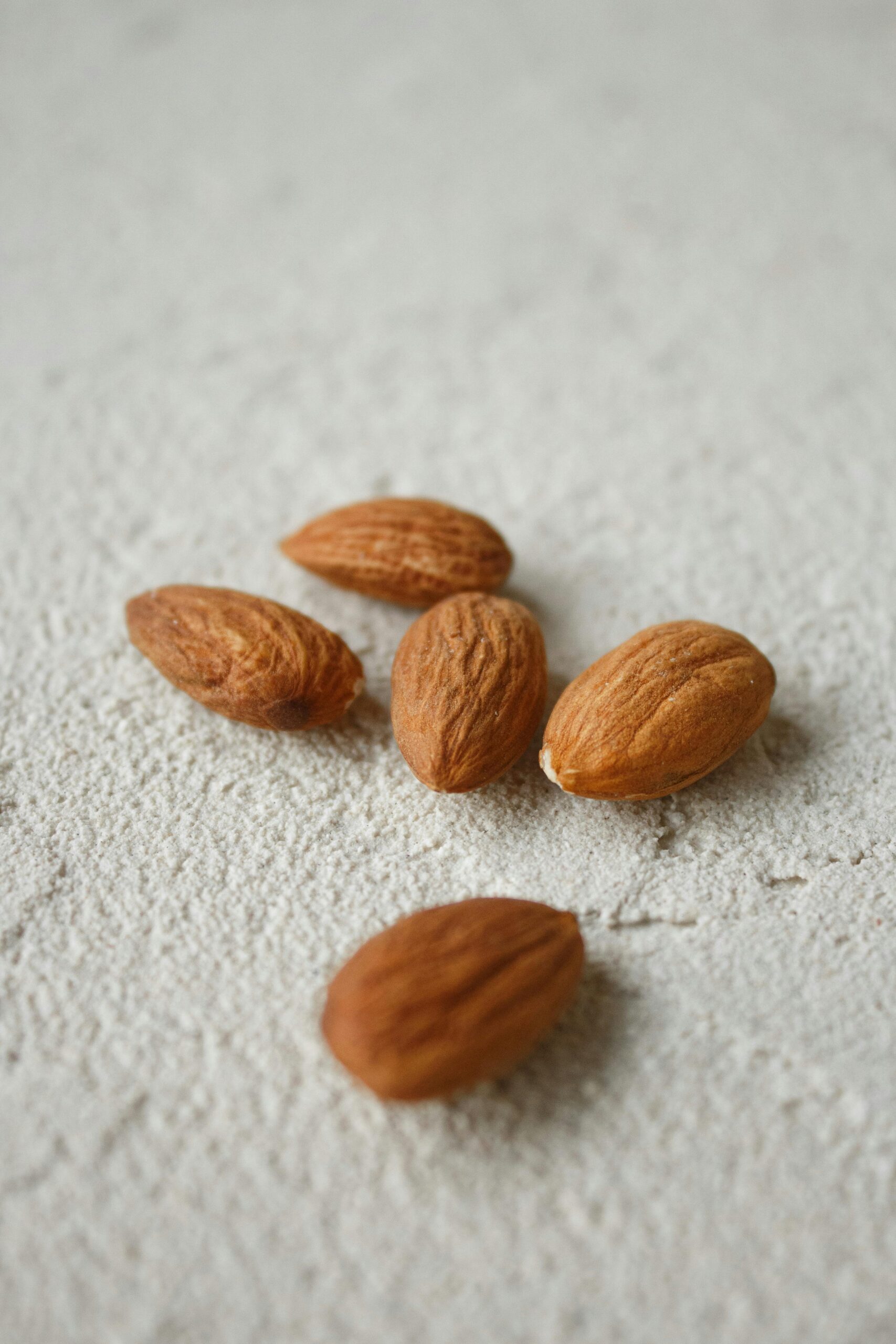 pexels-photo-7625229-7625229 Five almonds scattered on a light textured surface, captured in natural light.