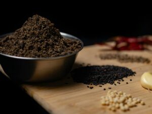 Close-up of assorted spices including black sesame and garlic on a wooden board.