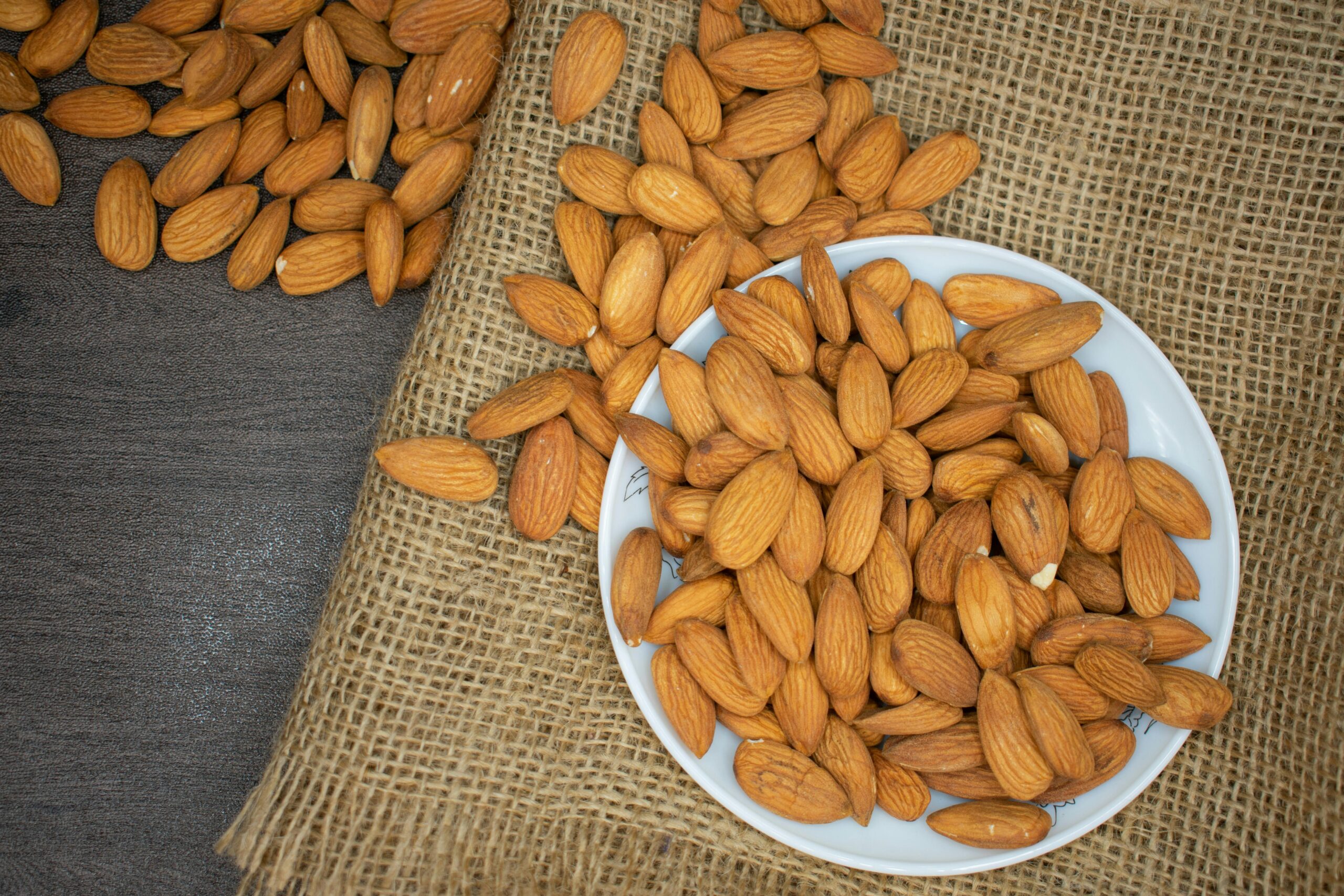 pexels-photo-3997459-3997459-1 Top view of almonds in a white bowl on a burlap surface, highlighting healthy snacking.