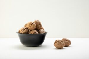 pexels-photo-7333062-7333062 A classic arrangement of whole walnuts in a black bowl on a white surface, offering elegant culinary visuals.